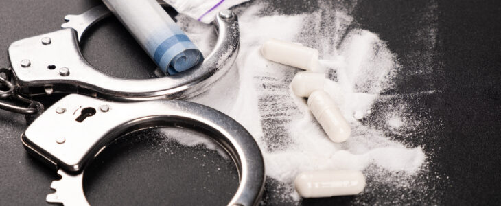 handcuffs and white powder drugs on a black background