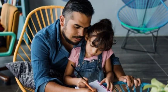 Hispanic man with young daughter writing on a notebook