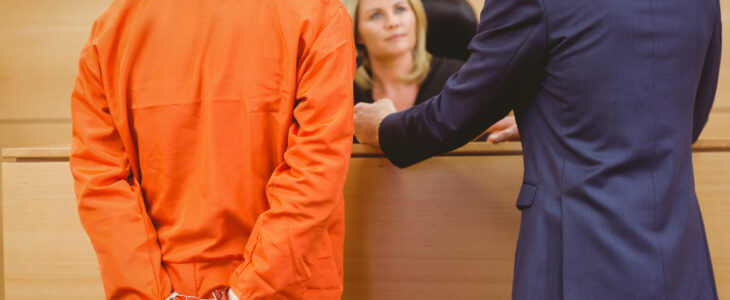 Lawyer and judge speaking next to the criminal in handcuffs in the court room